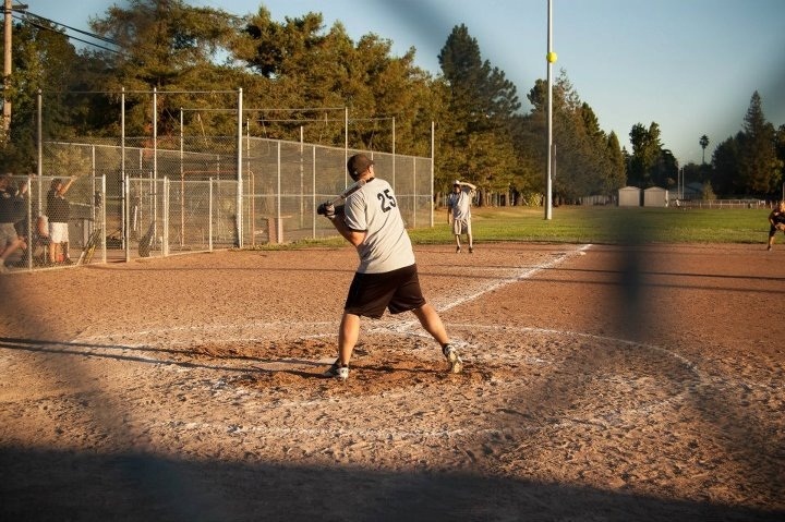 Adults participating in a softball game on a dirt field
